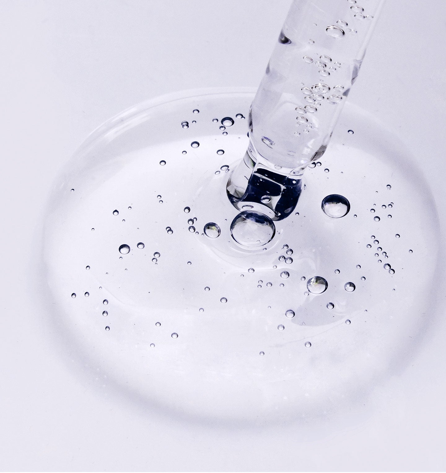 Clear liquid being poured into a glass with bubbles on a light gray background