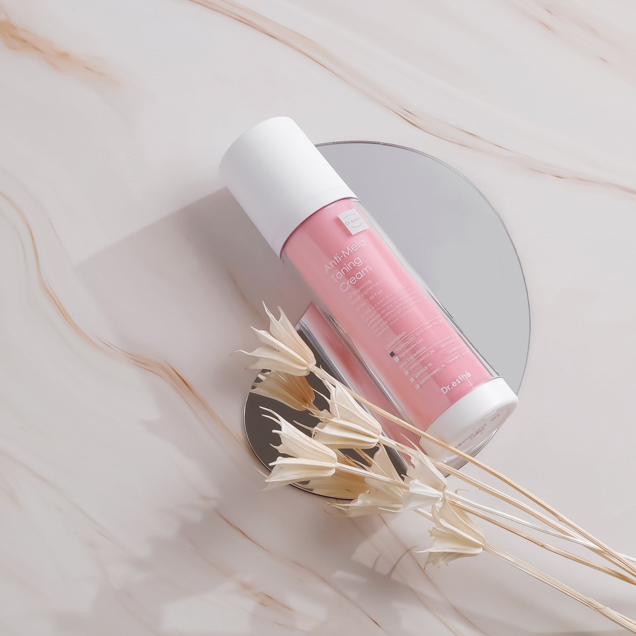 Pink and white cosmetic tube on a marble surface with dried flowers