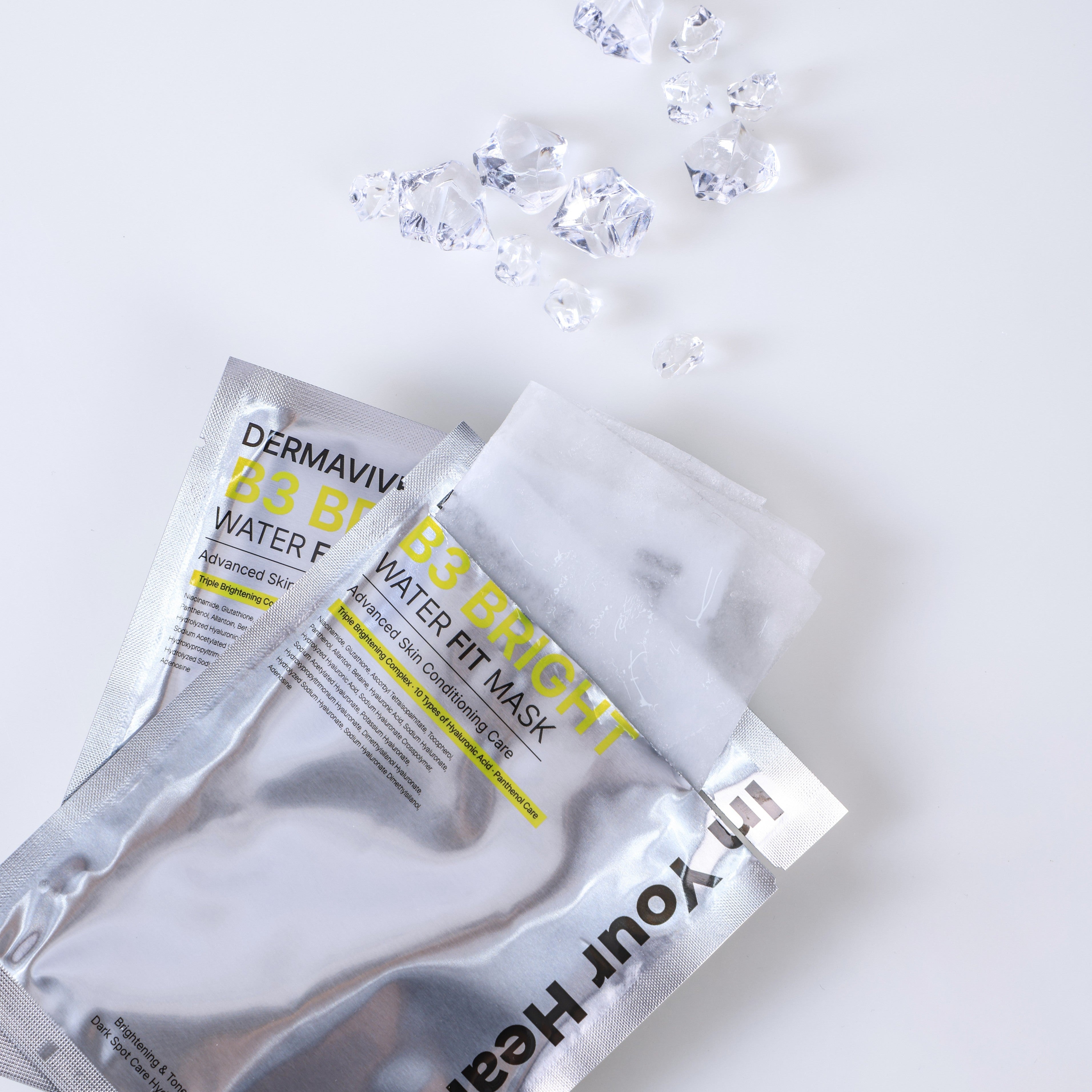Two silver packets of In Your Heart DermaVive B5 Bright Water Fit Mask are arranged on a white background with a few clear faceted gemstones scattered above them.