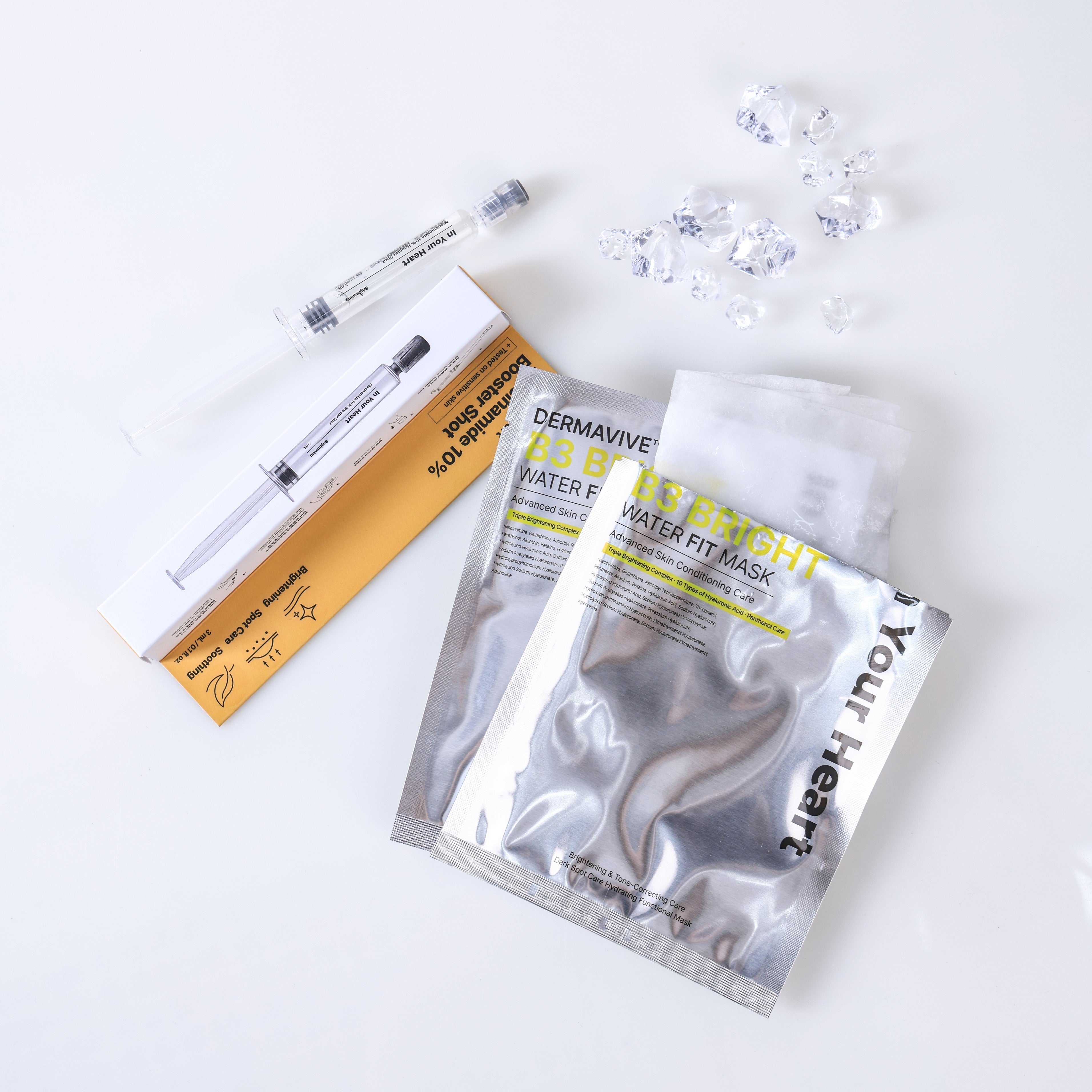 A skincare set laid out on a white background, including a silver foil packet labeled 'In Your Heart DERMAVIVE B3 Water Fit Mask', a clear syringe-like applicator in a white and gold box, and several small clear gel drops.