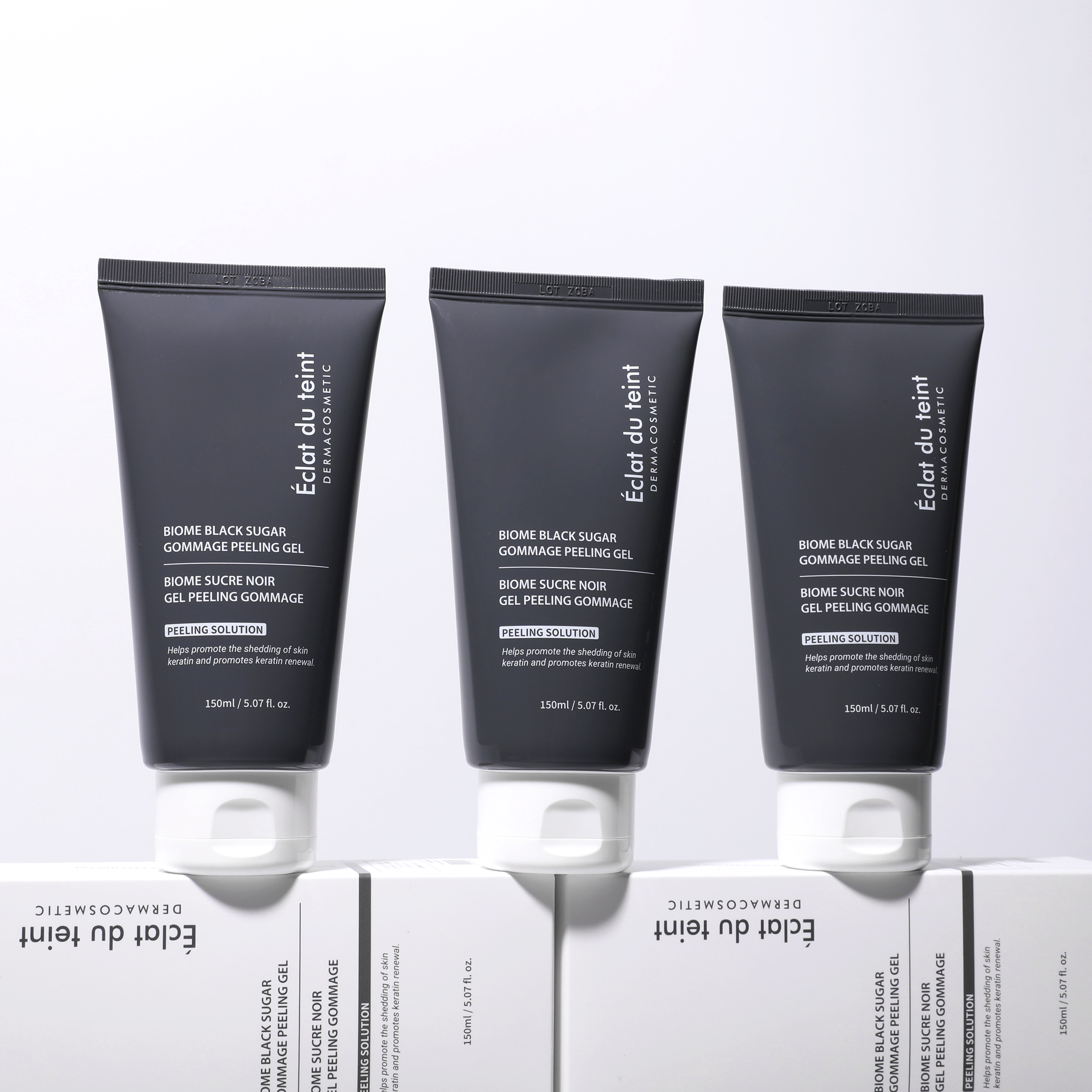 Three black tubes of Eclat du Teint skincare product Biome black sugar gommage peeling gel on a white background