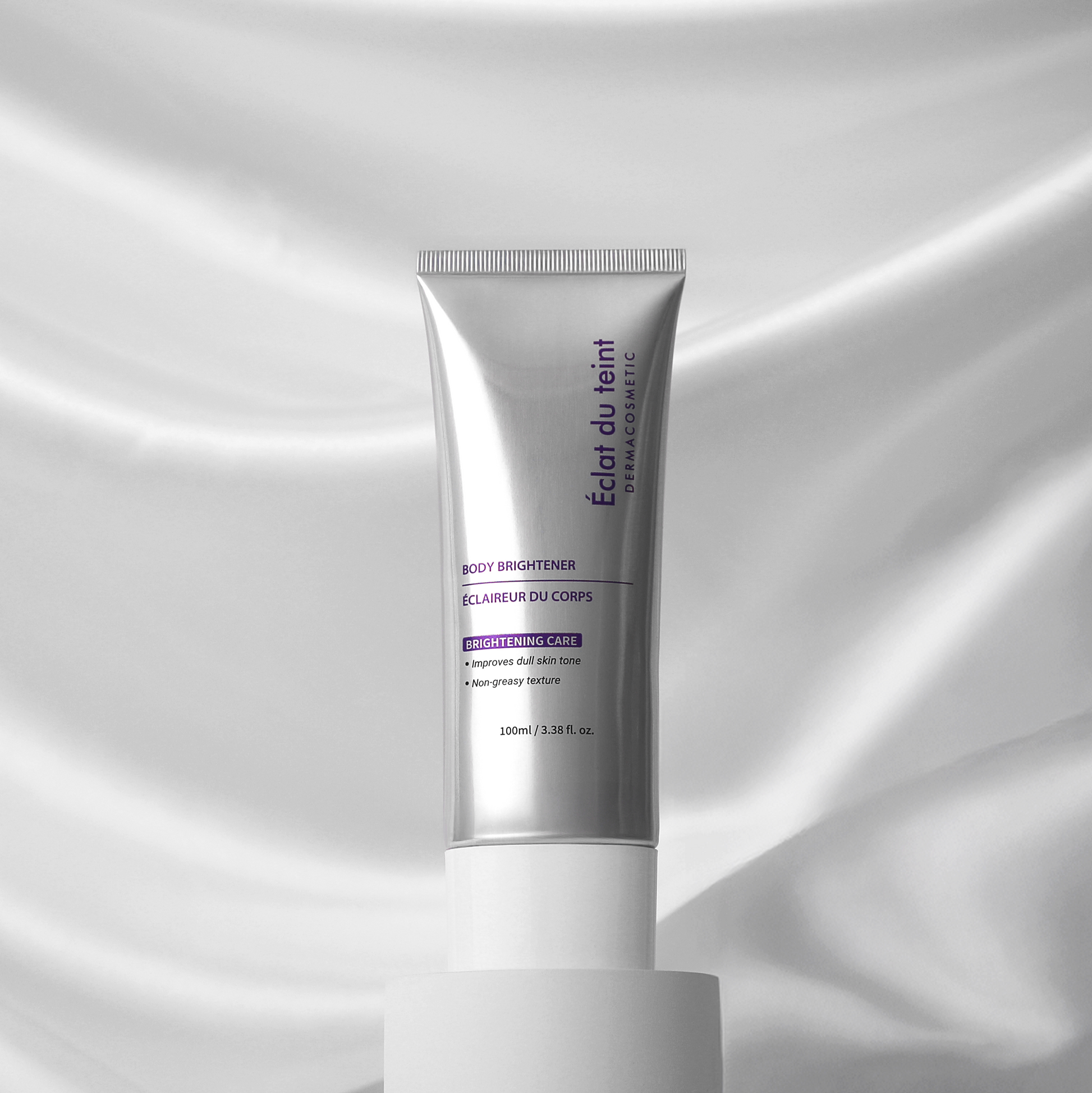 Skincare tube labeled 'Eclat du teint body brightener' on a white fabric background