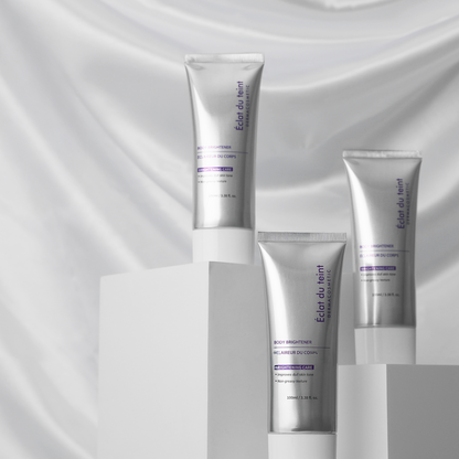 Three silver skincare bottles of Eclat du teint body brightener purple labels on a gray fabric background